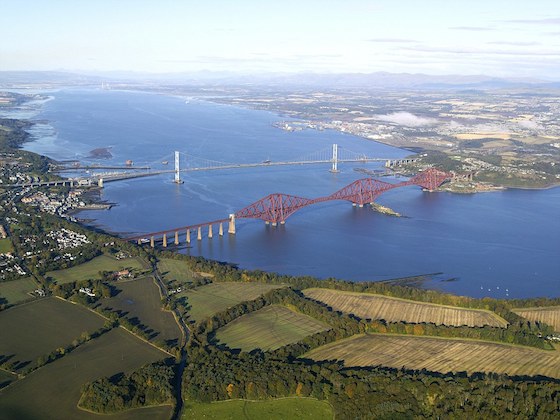 The Forth Bridges with South Queensferry far left, North Queensferry at the Fife landfall of the bridges on the north shore of the Firth of Forth, and the Rosyth Dockyard just above centre in this view. Work has already begun on the new Forth Crossing, and some of the caissons for the new bridge can be seen extending from the southern shoreline just beyond the Forth Road Bridge.